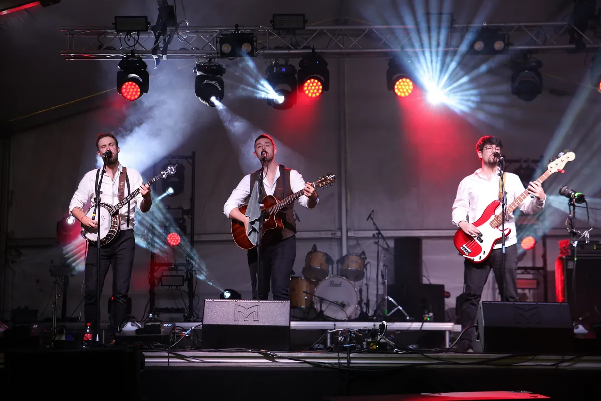 Fergus, Antony and Jamie singing together on stage under red and white spotlights