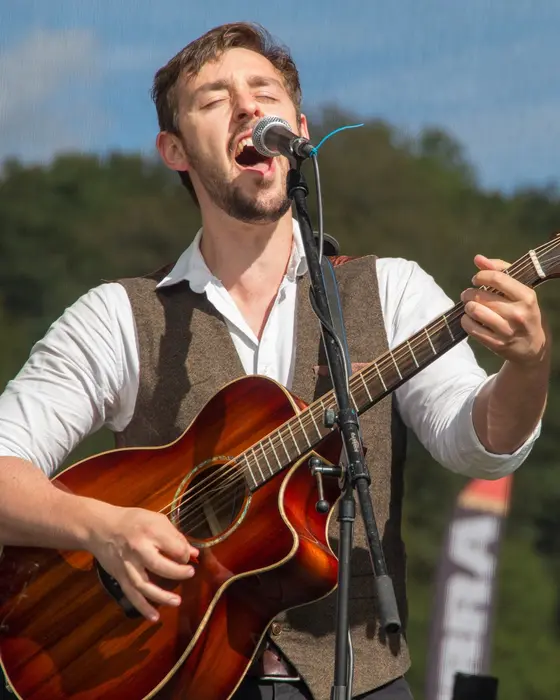 Antony singing with his guitar on an outdoor stage